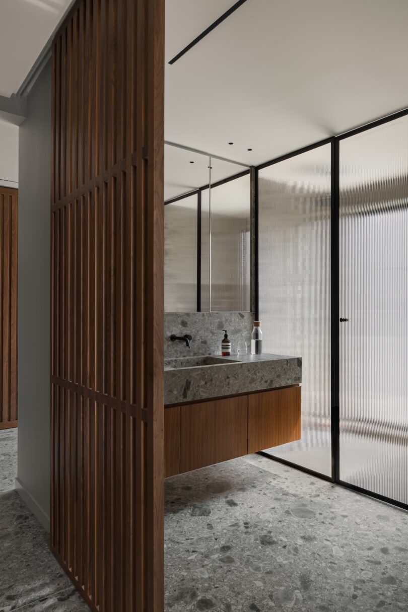 Modern bathroom with terrazzo flooring, a floating stone vanity with wooden accents, and glass partition walls.