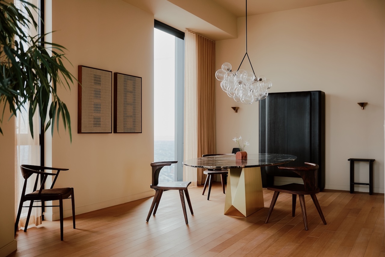 El moderno comedor cuenta con una mesa redonda de mármol, cuatro sillas de madera, una base dorada geométrica, un moderno candelabro de burbujas, dos obras de arte enmarcadas y un gabinete alto negro.