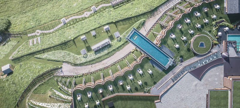 Una vista aérea del área de la terraza al aire libre, completa con piscina lineal, tumbonas, vegetación, senderos y elementos paisajísticos modernos, que refleja el diseño innovador de la extensión del spa del Hotel Hubertus.