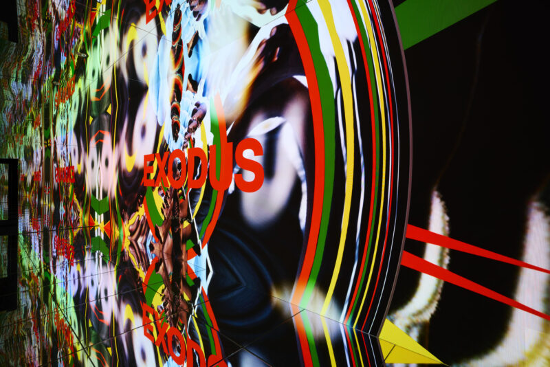 A digital, mirrored wall displays the word "EXODUS" in red amid colorful abstract patterns and reflective surfaces.