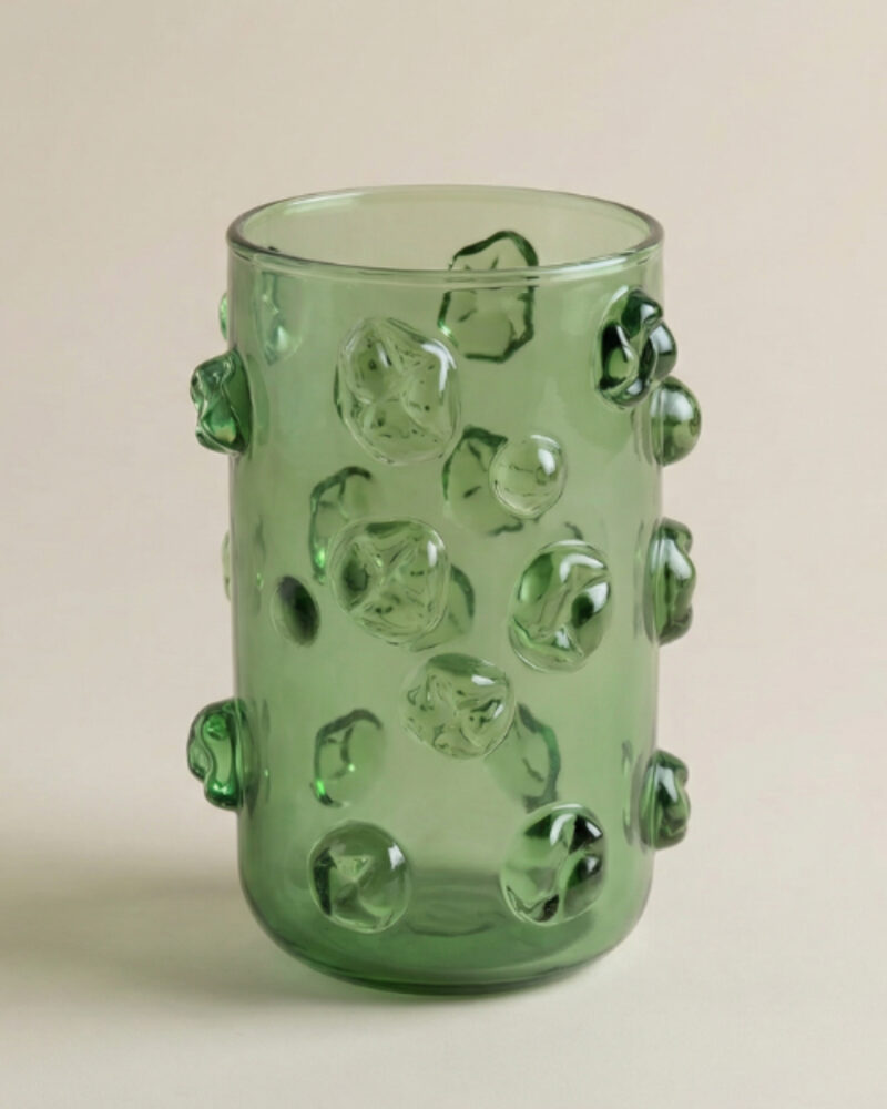 Green glass tumbler with a cylindrical shape and raised, irregularly shaped bubble-like protrusions on its surface, on a plain background - a striking piece that beautifully incorporates the vibrant textures of Modern African Decor.