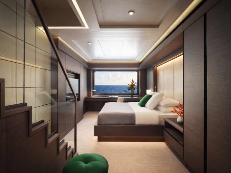 Modern yacht bedroom with large bed, desk, and window overlooking the ocean; staircase leads upstairs, and tropical flowers decorate the room.