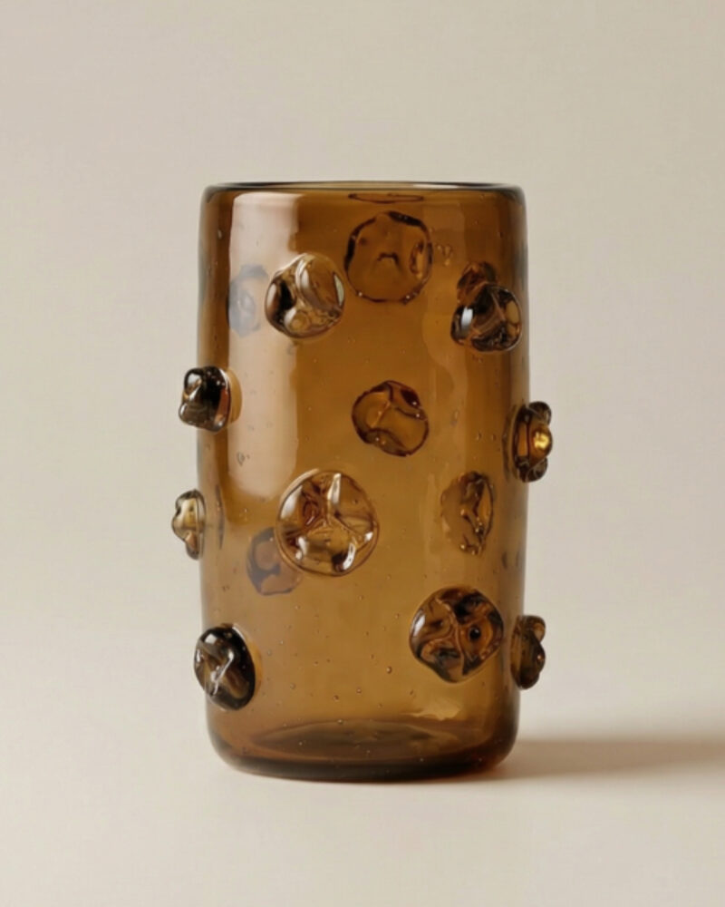 A cylindrical brown glass vase with raised, rounded decorative bumps evenly spaced across its surface, against a light background—an elegant piece that beautifully incorporates modern African decor.