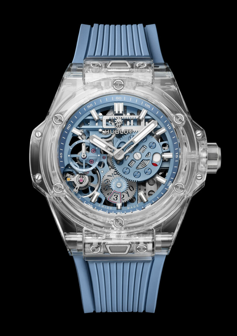 Skeleton watch with a transparent case, blue accents, and a blue rubber strap, displaying intricate inner mechanics on a black background.