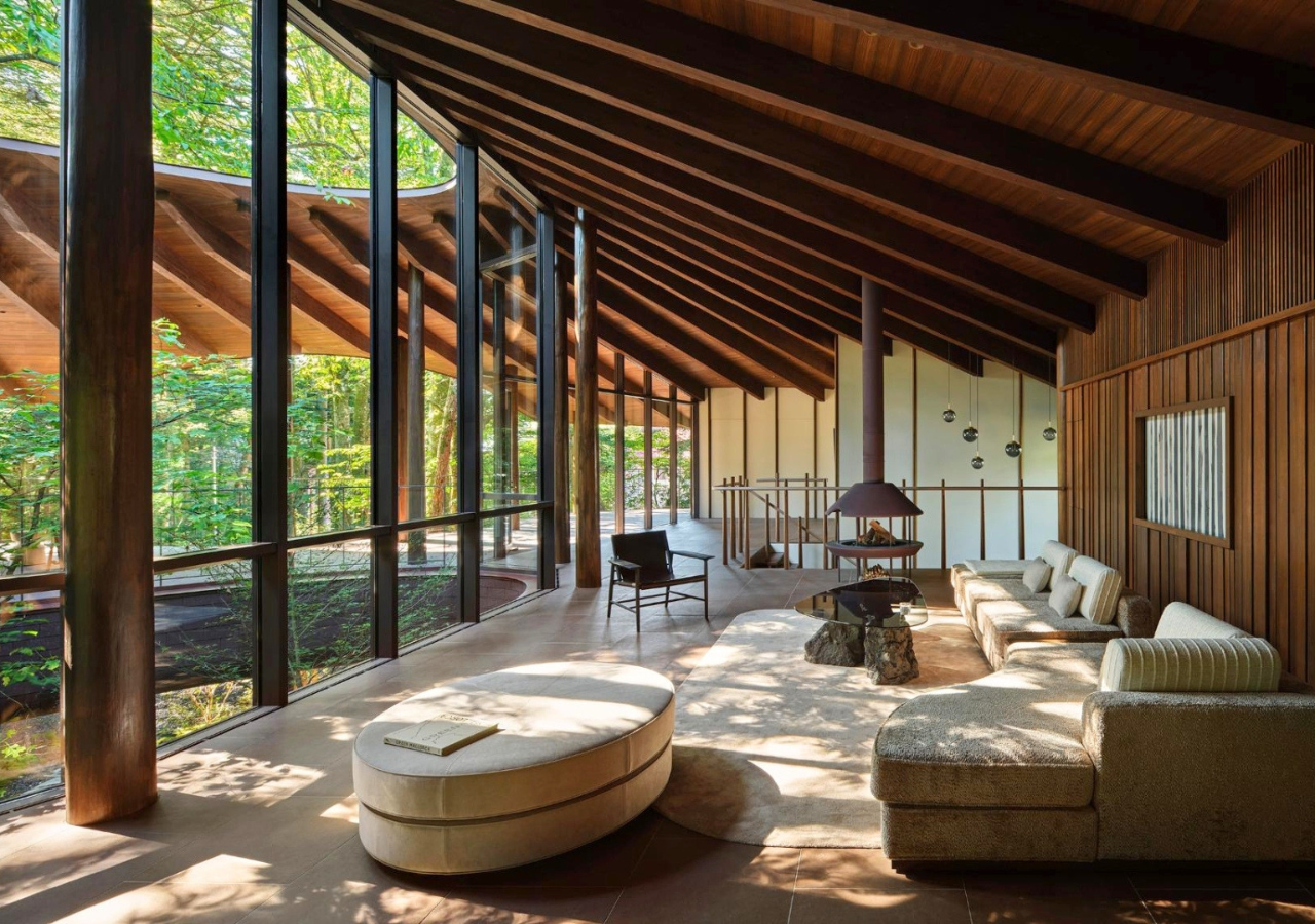 Modern living room with floor-to-ceiling windows, wooden ceiling beams, neutral furniture, and forest view outside. Natural light fills the space, creating an atmosphere worthy of an iF DESIGN AWARD.