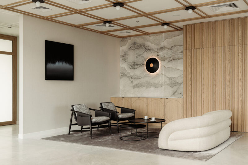 Modern lounge in the Baker McKenzie Warsaw office features a curved white sofa, black chairs, marble wall accent, wood paneling, minimalist decor, and abstract artwork.
