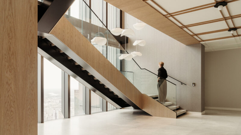 A person stands at the top of a modern indoor staircase with glass railing in the Baker McKenzie Warsaw office, surrounded by large windows and contemporary light fixtures.