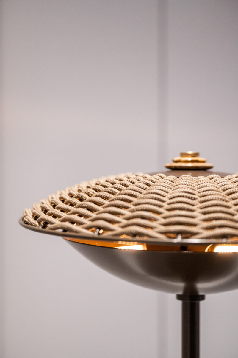 A close-up of a decorative woven lampshade on a metallic stand, with a neutral background and soft lighting.