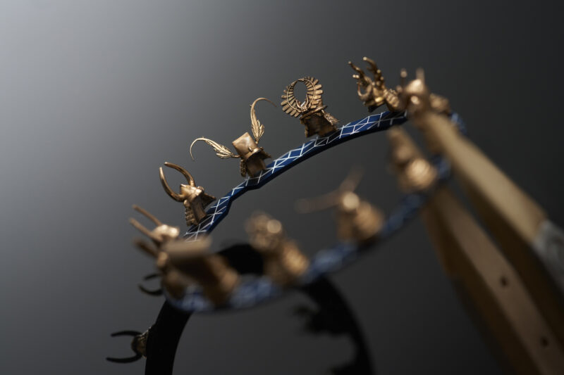 A Roger Dubuis Excalibur crown decorated with small, golden miniature helmets, held by a pair of metal tweezers.