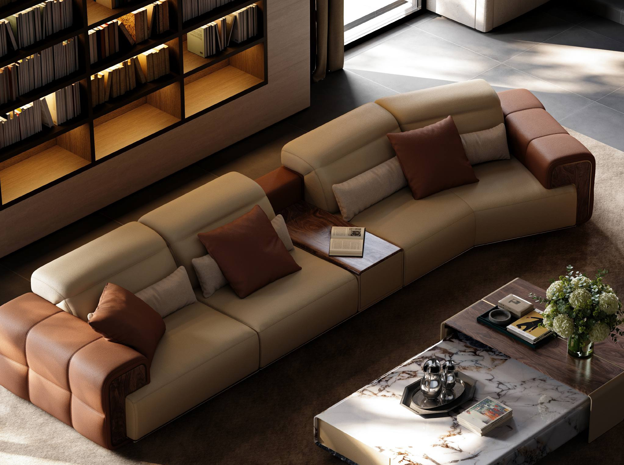 High-angle view of a modern curved sofa in ivory upholstery with tobacco leather ends, a stone coffee table, and a built-in bookshelf.