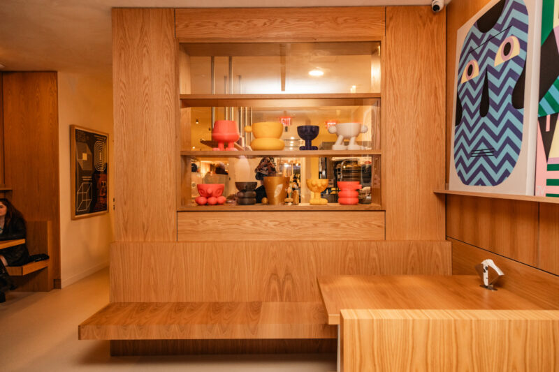 A wooden wall at Softville NYC featuring a recessed shelf with colorful, stylized character figurines above a built-in bench.