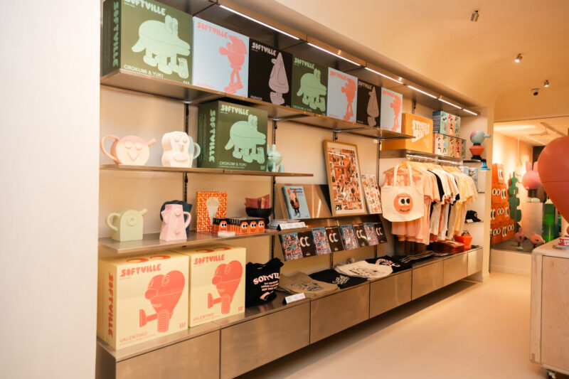 Shelves in a Softville NYC store display character-themed boxes, ceramics, illustrated prints, and branded apparel.