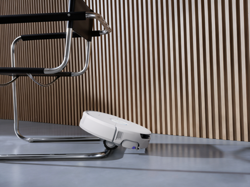 A white Narwal Flow 2 robot vacuum cleaner maneuvering around the chrome leg of a chair.
