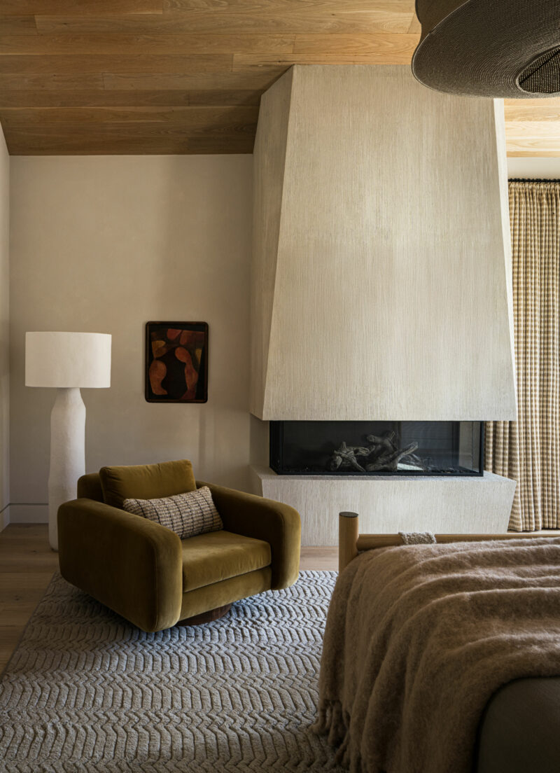 A modern room with a large textured fireplace, an olive green armchair, and a bed.