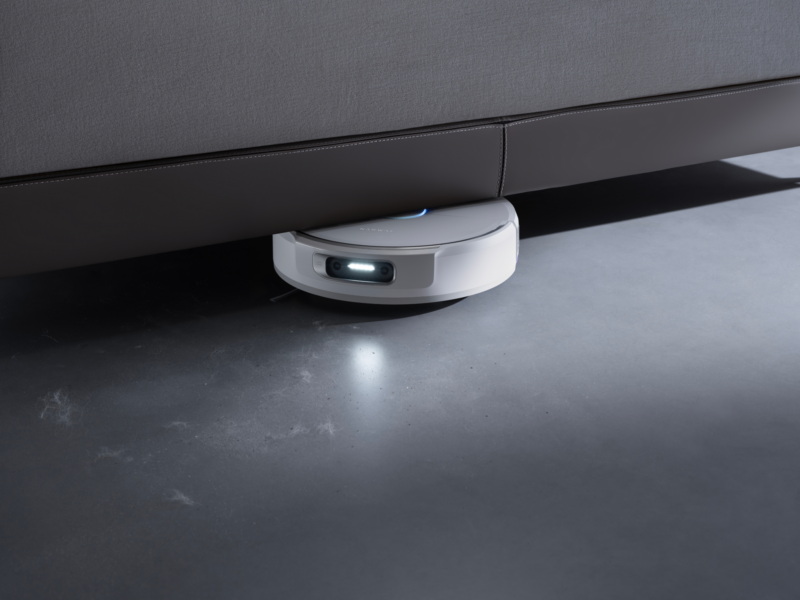 A white Narwal Flow 2 robotic vacuum cleaner cleaning under a sofa.