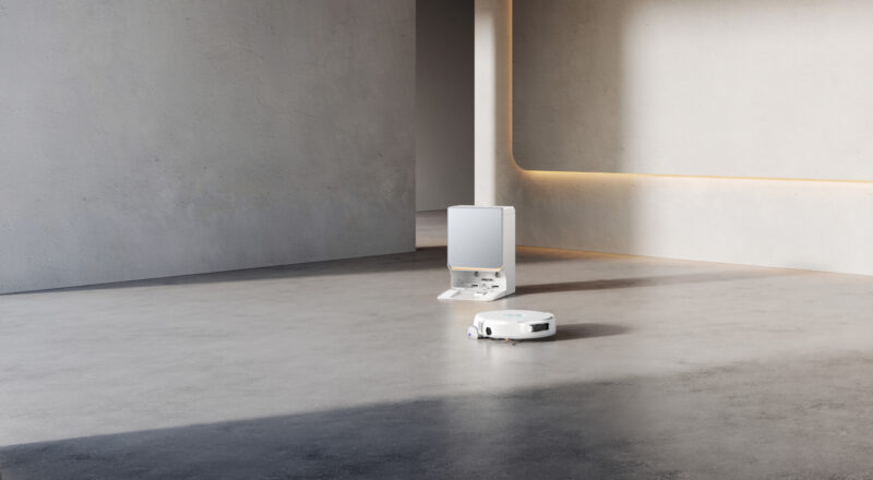 A white Narwal Flow 2 robot vacuum cleaner sits on a concrete floor in front of its docking station.