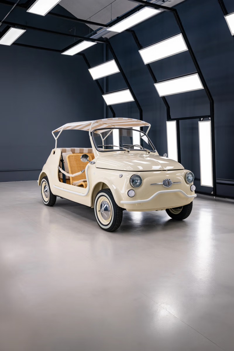 A cream-colored Garage Italia Fiat 500 Spiaggina beach car with a striped canopy top and wicker-style seats.