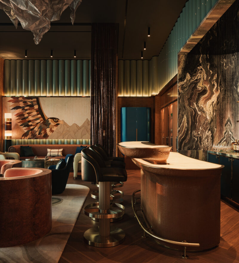 A bar area with a curved, metal-textured counter and stools, featuring a mural of a falcon on the wall and marble accents.
