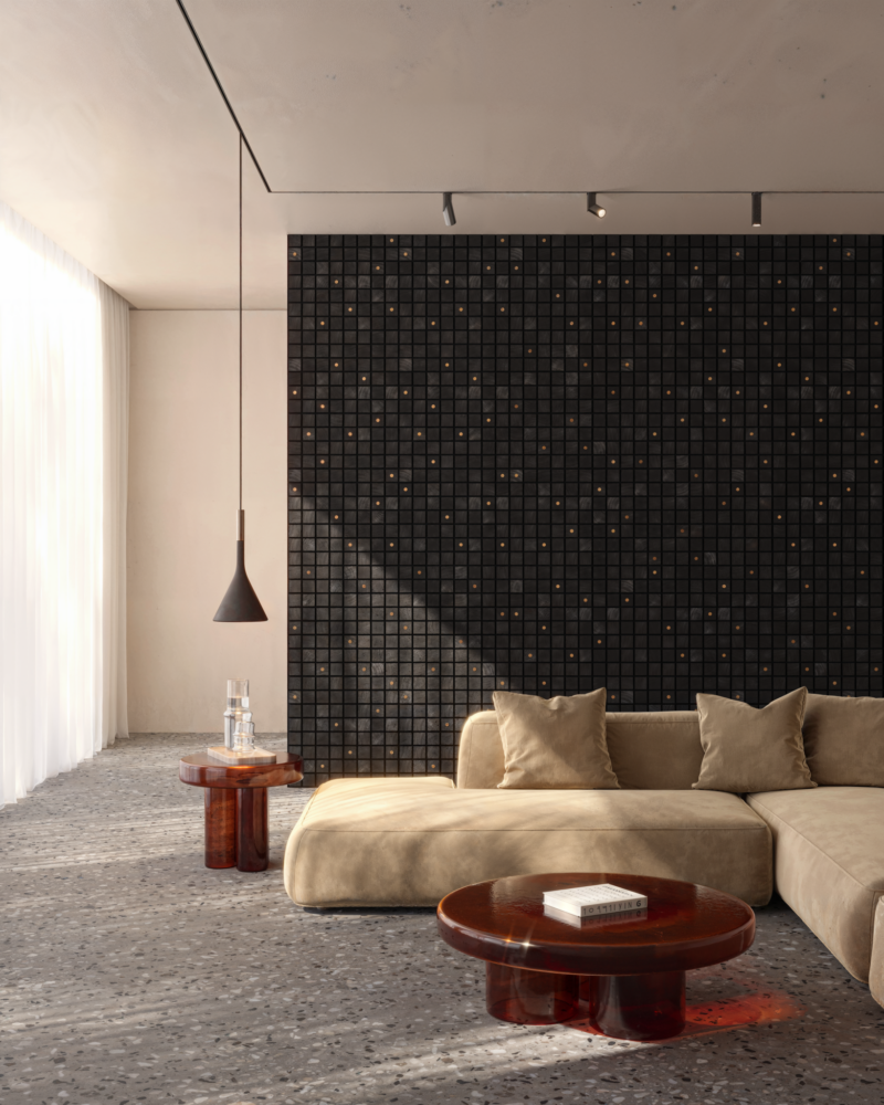 A beige sectional sofa by Alfonso Verduzco sits in a room with a black mosaic tile feature wall, a low amber-colored circular coffee table, and terrazzo flooring.