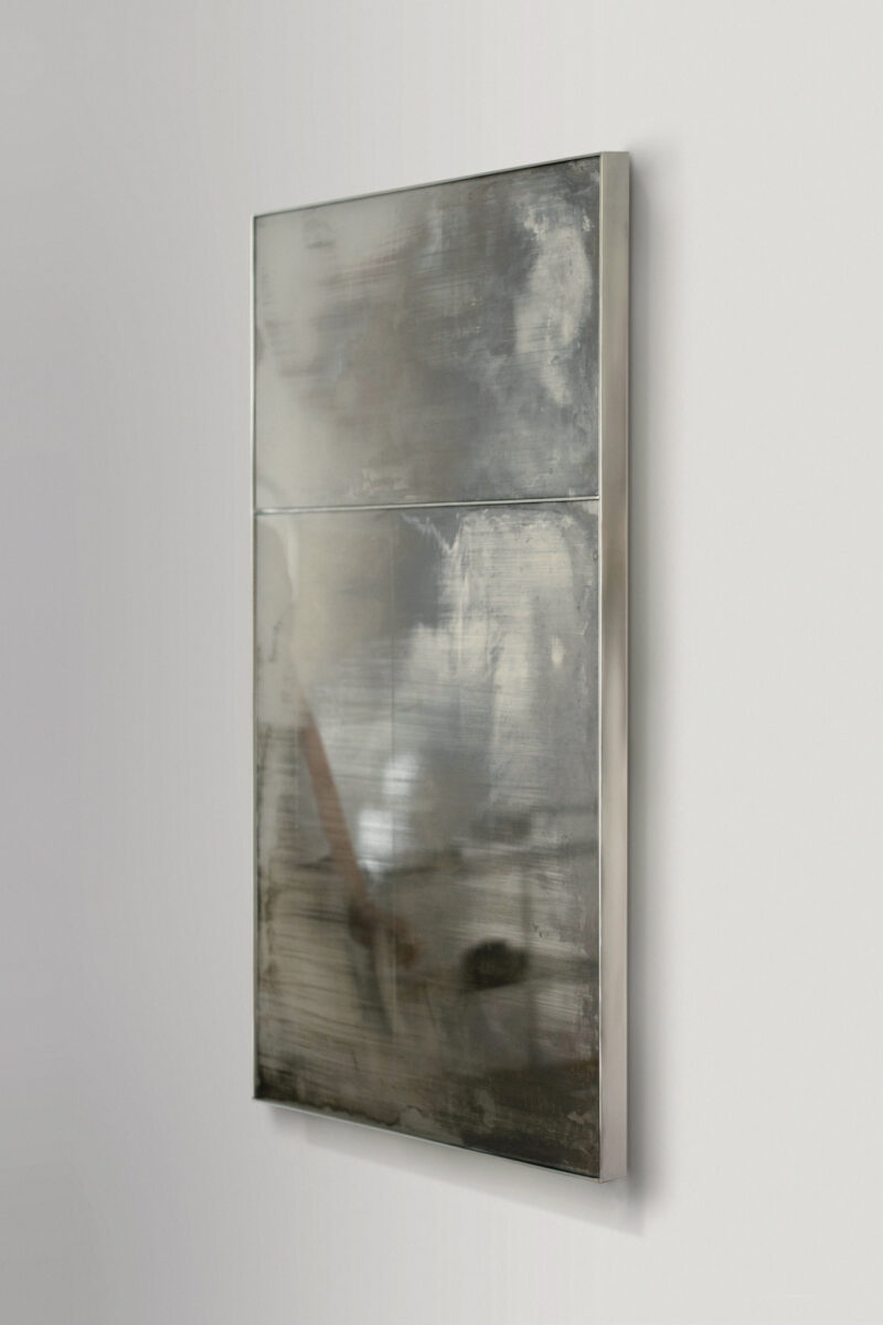 A rectangular, silver-framed mirror with a distressed, cloudy surface, mounted on a white wall.
