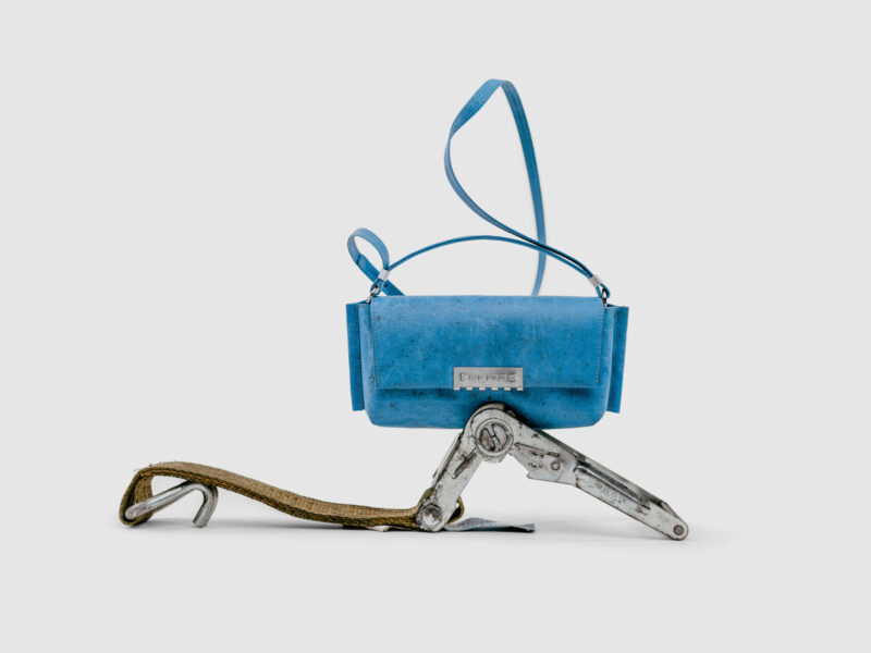 A blue rectangular shoulder bag from the Freitag Reference collection, balanced on a metal ratchet strap assembly.