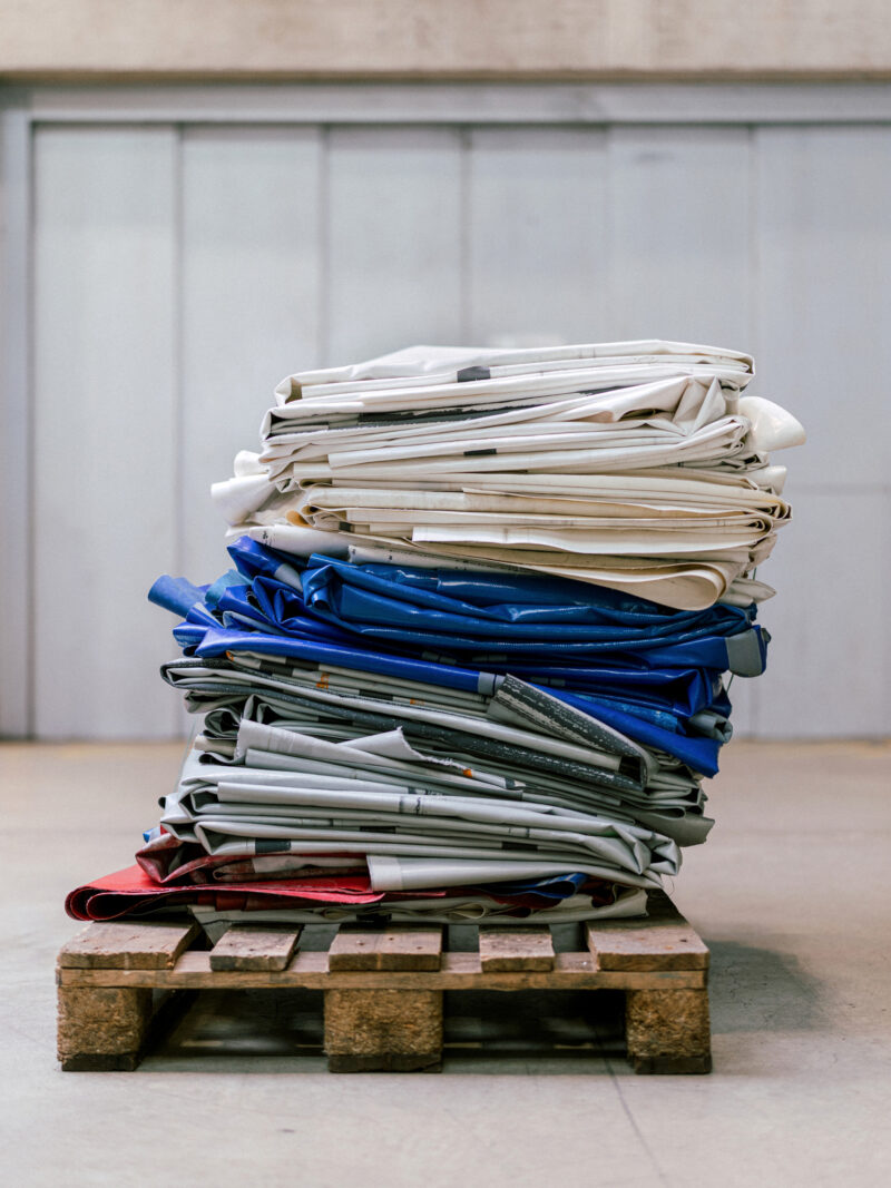 A stack of folded white, blue, and red Freitag Reference collection tarps on a wooden shipping pallet.