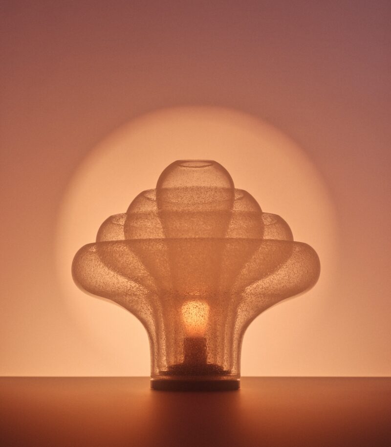 A sculptural frosted glass table lamp illuminated from within against a glowing circular background.