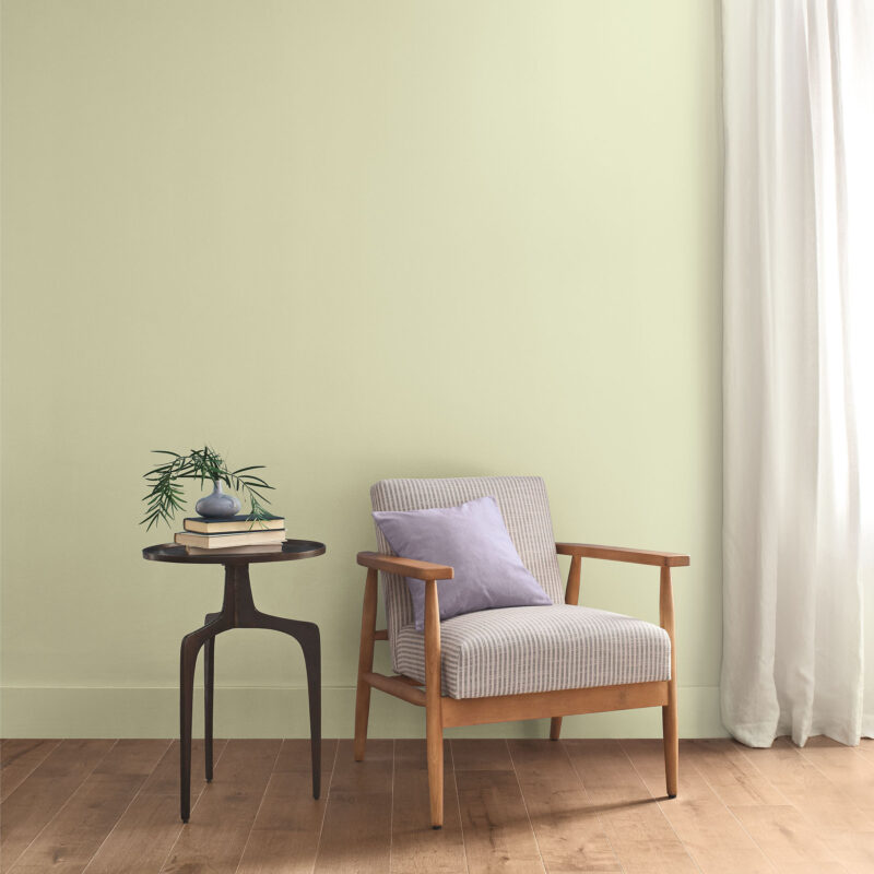 A striped armchair in the Sherwin-Williams 2027 Color of the Year with a purple pillow next to a round side table holding a stack of books and a small vase.