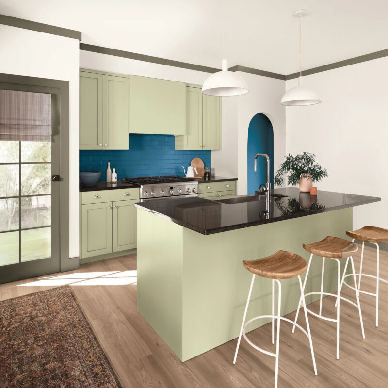 Kitchen with Sherwin-Williams 2027 Color of the Year sage green cabinets, a dark countertop island with three wooden stools, and a blue tiled backsplash.