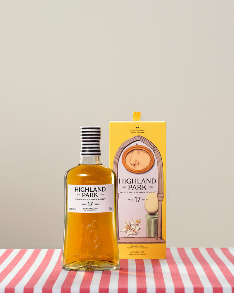 A bottle of Highland Park 17 Year Old Scotch whisky stands beside its decorative yellow box on a red-and-white striped surface.