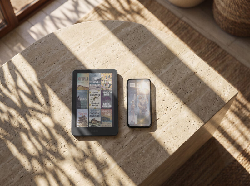 A Kindle redesign featuring a library of book covers on an e-reader next to a smartphone on a stone table.