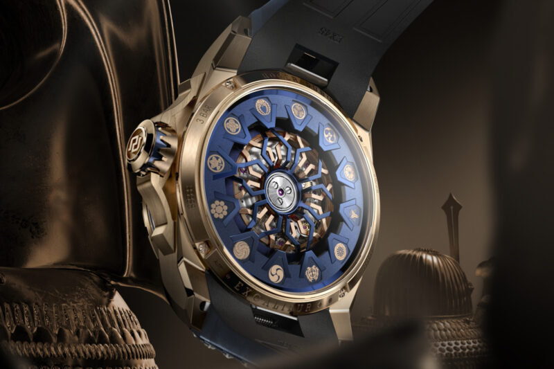 Roger Dubuis Excalibur watch with a rose gold case, blue dial featuring engraved circular motifs, and a black strap.