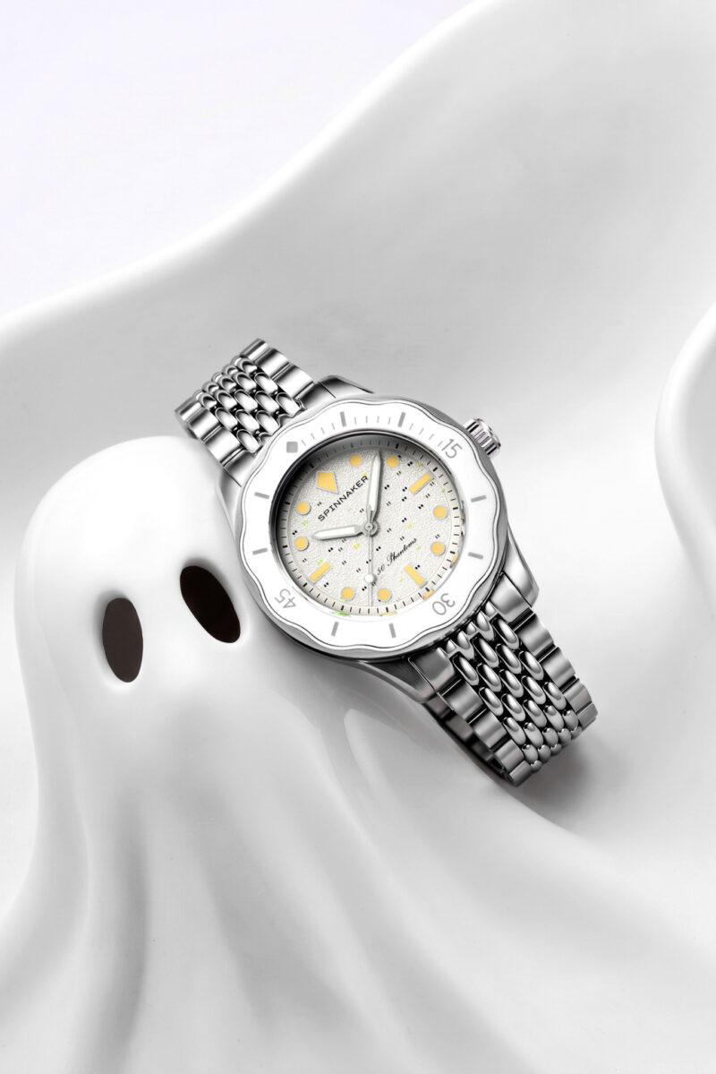 Spinnaker 50 Phantoms watch with a silver link band and textured white dial, resting on a white ghost-shaped sculpture.
