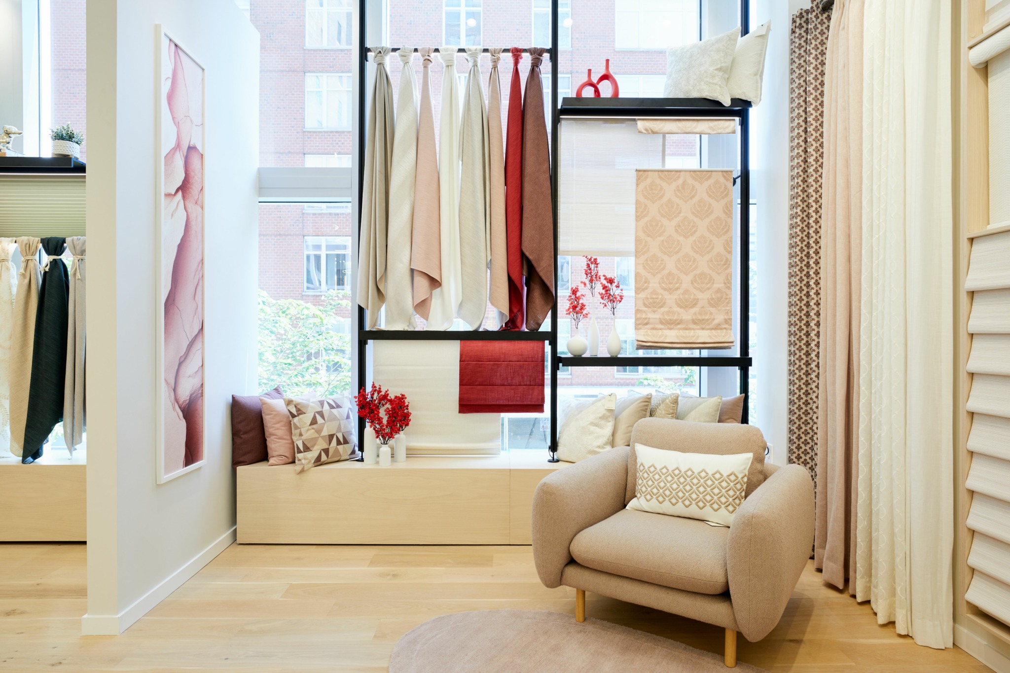 A showroom display featuring draped fabric samples, a beige armchair with a patterned pillow, and assorted window treatments.