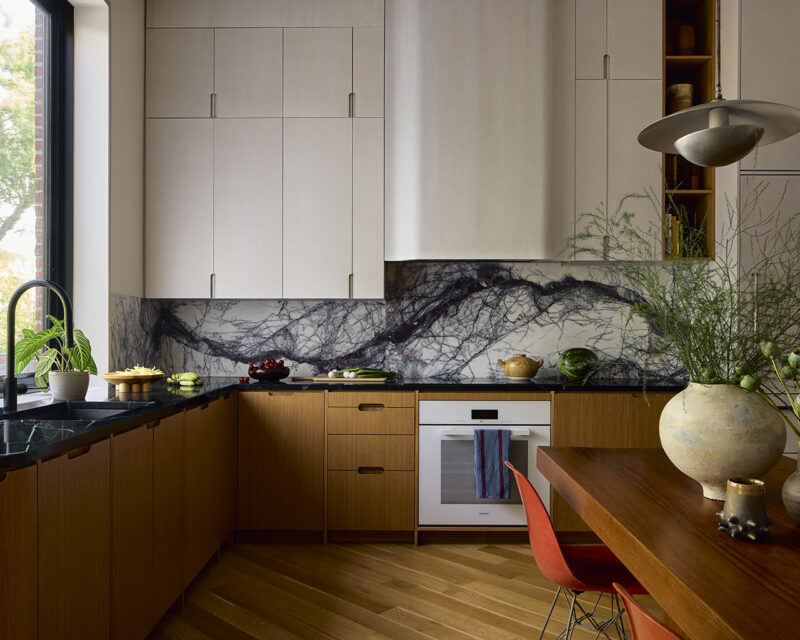 Modern kitchen with wood lower cabinets, light upper cabinets, and a prominent black and white marble backsplash.