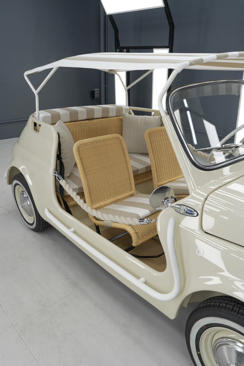 Cream-colored vintage Garage Italia Fiat 500 Spiaggina beach car with wicker seats, striped cushions, and a canopy top.