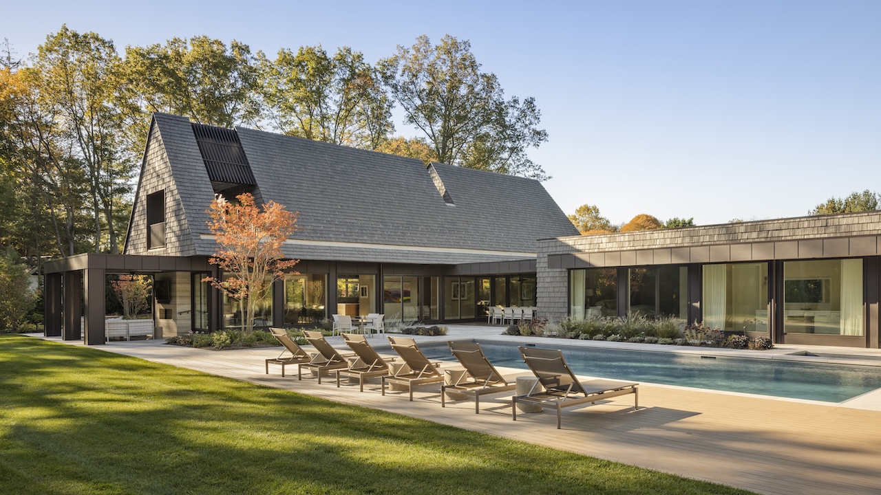 Modern house with a pitched shingle roof, a patio with lounge chairs, and an outdoor swimming pool.